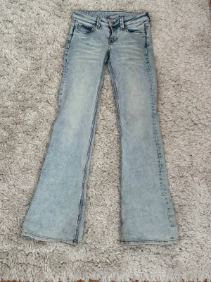 Bootcut ljusblå jeans från Cheap Monday - Säljer ett par ljusblå bootcut jeans från Cheap Monday med klassisk femficksdesign och en grymt snygg tvätt. Jeansen har en grön Cheap Monday-patch bak i midjan och är tillverkade i slitstarkt denim. Modellen är booty bei.