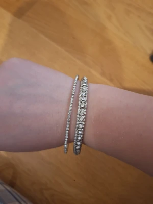Vintage silverfärgade bangel armband - Två snygga armband i silverfärg, båda med gnistrande stenar runt om. Det ena är smalare och diskret, medan det andra är bredare med större stenar för extra bling. Perfekta att bära tillsammans för en cool och trendig look.