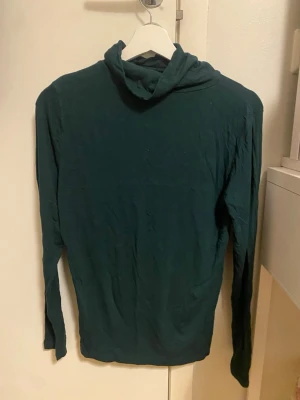 Mörkgrön polotopp i bomull - En enkel och stilren mörkgrön polotopp med lång ärm. Tillverkad i mjuk bomull och har en klassisk polokrage som ger en clean look. Perfekt att bära som lager eller för sig själv till jeans eller kjol.