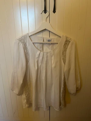Vit blus med spets från Vero Moda - Säljer en vit blus från Vero Moda i storlek M. Blusen har fina veck framtill, spetsdetaljer längs axlarna och trekvartsärmar. Säljer pga är för stor💘