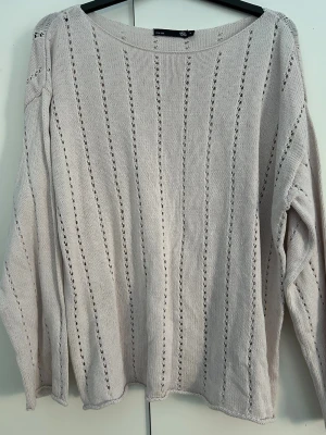 Beige stickad tröja från 157 - Säljer en beige stickad tröja från 157 med lång ärm och snygga hålstickade ränder längs hela tröjan. Tröjan har en avslappnad passform och rund halsringning, perfekt för lager på lager under vår.