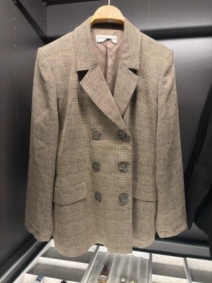 ✨ Vintage kavaj från Yves Saint Laurent ✨ - Vintage Yves Saint Laurent dubbelknäppt kavaj i beige/brunt rutigt tyg. Klassisk YSL-silhuett med breda slag och marmorerade knappar. Mycket hög kvalitet med fint fall och struktur – ett tidlöst statement-plagg som funkar både uppklätt och casual. Mycket fint vintage-skick. Nyvärde på liknande YSL-plagg ca 25 000–30 000 kr. 
