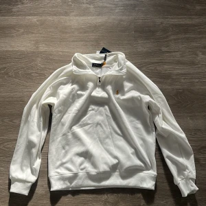 Vit half zip tröja från Polo Ralph Lauren - Vit långärmad tröja från Polo Ralph Lauren med klassisk gul broderad logga på bröstet. Tröjan har en stilren half zip-dragkedja och hög krage. Tillverkad i mjuk bomull för en clean och fräsch look. Perfekt för dig som gillar enkel och tidlös stil. Den är storlek m men passar s 