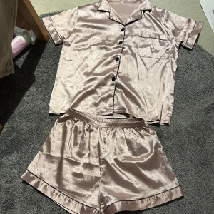 Champagnefärgade satinskjorts S - Säljer ett par glansiga champagnefärgade satinskjorts med elastisk midja och svarta kantdetaljer. Perfekta för chill hemma eller som pyjamas. Matchar toppen i samma material och färg för en snygg helhet.
