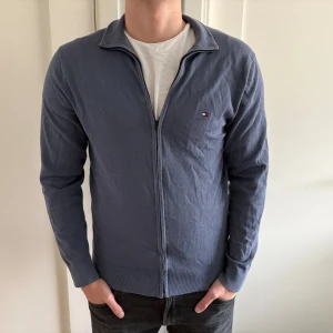Blå kofta från Tommy Hilfiger - Snygg blå kofta från Tommy Hilfiger med dragkedja framtill och liten logga på bröstet. Tröjan har lång ärm, ribbade muddar och klassisk krage. 