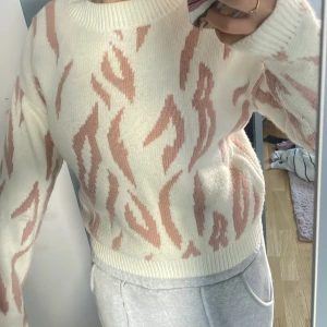 Vit och rosa stickad tröja med mönster - Superfin stickad tröja i vitt med ljusrosa zebramönster. Tröjan har rund halsringning, ribbade muddar och är långärmad. Perfekt för dig som vill ha en mysig och trendig look med lite extra attityd.