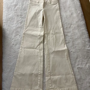 Randiga vida low waist byxor i beige bomull - Snygga beige byxor low waist med tunna vertikala ränder och riktigt vida ben. Byxorna har en klassisk passform upptill och faller ut i en cool wide-modell. Perfekta för dig som gillar en trendig och avslappnad look. Tillverkade i mjuk bomull för extra komfort.
