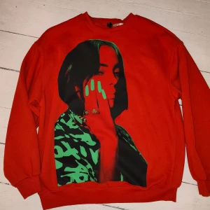 Röd Billie Eilish sweatshirt  - Röd sweatshirt från Divided med stort Billie Eilish-tryck i grönt och svart på framsidan och hennes namn i grönt på ryggen. Tröjan har rund hals och långa ärmar. Perfekt för dig som gillar Billie Eilish 