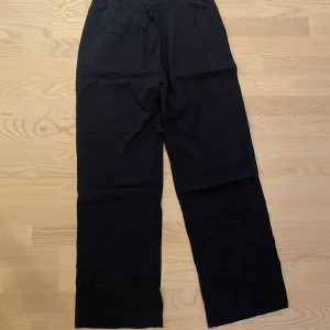 Oanvända svarta/mörkblå linnebyxor från 157, stl S - Oanvända svarta/mörkblå linnebyxor från 157 med avslappnad passform och dragsko i midjan. Byxorna har raka, vida ben och elastisk midja för extra komfort. Perfekta för en chill och stilren look.