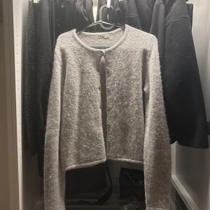 Grå fluffig kofta från Gina Tricot - Mysig grå kofta från gina med fluffig känsla och rund halsringning. Koftan har långa ärmar och knäpps med små knappar framtill. Perfekt för lager-på-lager och chill dagar.