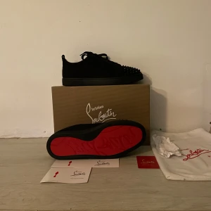 Christian Louboutin svarta sneakers med nitar - Säljer ett par svarta sneakers från Christian Louboutin med ikonisk röd sula och svarta nitar på tån. Skorna har snörning och är tillverkade i textil och skinn. Perfekta för dig som vill sticka ut med en edgy och lyxig stil. Köpt i usa Los Angeles📍gör för 500 USD som är runt 5000kr 🍾💸 säljer dom för dom är för små för mig.
