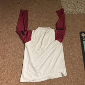 PSG x Jordan långärmad fotbollströja M - Säljer en PSG x Jordan långärmad fotbollströja i vitt med vinröda ärmar och svarta detaljer. Tröjan har guldigt Jordan-logga, PSG-märke på bröstet och dragkedja vid halsen. Tillverkad i lätt och ventilerande polyester, perfekt för träning eller match.