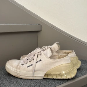 Vita sneakers Calvin Klein Jeans - Snygga vita sneakers från Calvin Klein Jeans med genomskinlig, chunky sula och klassisk snörning. Skorna har en stilren design med logga på sidan och plös, samt ovandel i canvas. Perfekta för dig som gillar en modern och clean look. Använda 2-3 gånger det är lätt att få bort fläckarna på de.