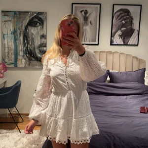 Vit broderad kortklänning från Nelly - Superfin vit kortklänning från Nelly med broderade detaljer och volangkant. Klänningen har långa puffärmar, v-ringning och markerad midja. Perfekt för sommarens alla tillfällen. Söt spetskant nertill och snygg struktur i tyget.