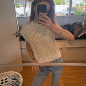 Vit stickad ärmlös tröja - Säljer en vit stickad tröja med korta ärmar och klassiskt flätmönster. 