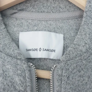 Grå ulljacka från Samsøe Samsøe - Snygg grå jacka från Samsøe Samsøe i mjuk ullmix. Jackan har rak passform, lång ärm och hel dragkedja framtill. Enkel och stilren design utan krage, perfekt för lager-på-lager. Passar dig som gillar minimalistisk och clean stil.