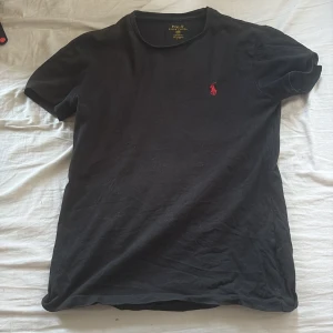 Svart t-shirt Polo Ralph Lauren XS - Svart t-shirt från Polo Ralph Lauren i custom fit med klassisk röd broderad logga på bröstet. T-shirten är kortärmad och tillverkad i mjuk bomull, perfekt för en clean och stilren look.