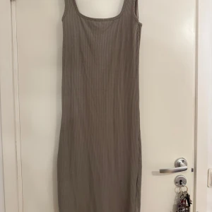 Beige ribbad långklänning - Säljer en beige ribbad långklänning med ärmlös design och fyrkantig ringning. Klänningen har en tight passform och är tillverkad i mjuk bomullsmix som känns skön mot huden. Perfekt för dig som gillar stilrena och enkla plagg med en modern touch.