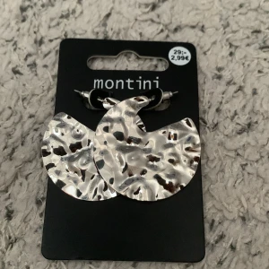 Silvriga örhängen från Montini - Säljer ett par coola silvriga örhängen från Montini med hamrad yta och rund form. Perfekta för att ge din look lite edge och glans. Snygga att matcha med både streetwear och trendiga outfits. Helt nyaa