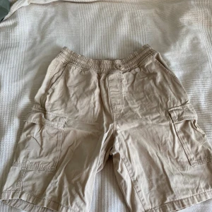 H&M beige cargoshorts herr - Säljer ett par beiga cargoshorts från H&M loose fit med elastisk midja. Fickor fram och på sidan