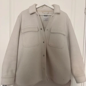 Beige overshirt från Dobber XS/S - Säljer en beige overshirt från Dobber i storlek XS/S. Skjortan har en loose passform, två stora bröstfickor med lock och tryckknappar framtill. Materialet är mjukt och känns ulligt, perfekt för lager på lager. Snygg krage och rundad nederkant.