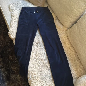 Mörkblå mjukisbyxor Juicy Couture XS - Mörkblå mjukisbyxor från Juicy Couture i supermjuk sammet. Byxorna har bred resår i midjan med snörning, stora fickor fram och bakfickor med knappar. Perfekta för en chill och trendig look. Säljer även en tröja till!