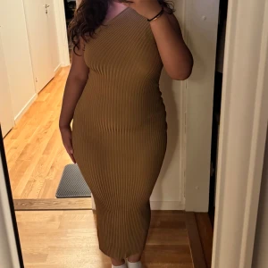 Ribbad brun långklänning från h&m - Säljer en snygg ribbad långklänning från H&M i brun/guld färg. Klänningen har oneshoulder-design och är figurnära med stretchigt material som framhäver formerna. Perfekt för dig som gillar stilrena och trendiga plagg med cool passform.