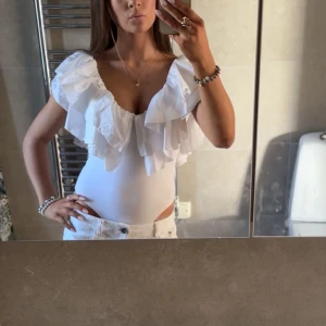 Vit volangbody ZARA - Supersnygg vit body med djup v-ringning och stora volanger över axlarna. Det är storlek M, men jag skulle säga att det är mer en S. Bodyn har en inte så synlig fläck vid höften då förra säljaren ljög om fläckarna så jag visste ej om dem när jag köpte bodyn tyvärr. Skriv vid funderingar!💞PRIS ÄR DISKUREBART!!!!😊🙏🏼