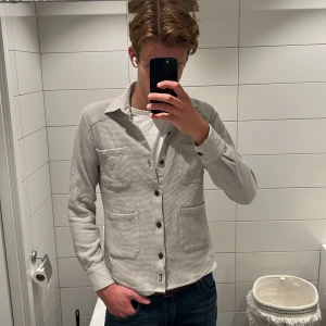Ljusgrå overshirt från Dahlin by Eberstål - Snygg ljusgrå overshirt från Dahlin by Eberstål i 100% ekologisk bomull. Skjortan har en strukturerad yta, fyra praktiska fickor framtill och knäppning med mörka knappar. Jag på bilden är 187cm. Denna kostar 1899 kr nypris. Hör gärna av er om ni vill ha mer bilder eller om ni har ett prisförslag 