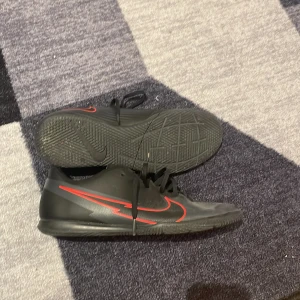 Nike fotbollsskor svart/röd strl 44 - Säljer ett par svarta Nike fotbollsskor med röda detaljer och klassisk swoosh på sidan. Skorna har snörning och platt sula med mönster för bra grepp på planen. Perfekta för dig som vill sticka ut med stilren design och sportig känsla.