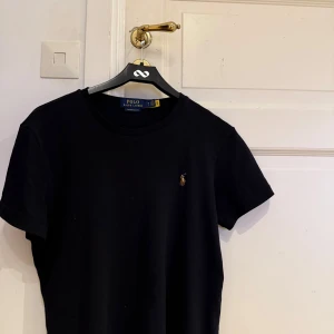 Svart t-shirt Polo Ralph Lauren - Svart t-shirt från Polo Ralph Lauren i custom slim fit. Klassisk design med rund hals och broderad logga på bröstet. Tillverkad i mjuk bomull, perfekt för en clean och stilren look.