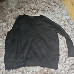 Svart stickad tröja med v-ringning - Svart stickad tröja från Kappahl i storlek L. Tröjan har v-ringad hals, långa ärmar och breda ribbade muddar vid ärmslut och nederkant. Materialet är 90% akryl och 10% ull, vilket gör den mjuk och skön att bära.
