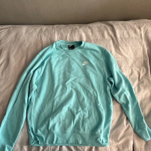 Turkos sweatshirt från Nike, storlek M - Fräsch turkos sweatshirt från Nike i storlek M. Tröjan har en klassisk rund hals och långärmade ärmar. Nike-loggan är broderad i vitt på bröstet. Mjuk insida och ribbade muddar vid ärmslut och nederkant. Perfekt för chill eller sport.