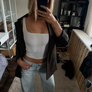 Vit ribbad linnetopp - Säljer en fräsch vit ribbad linnetopp med breda axelband och croppad passform. Toppen har en fyrkantig urringning och är tillverkad i ett stretchigt bomullsmaterial som sitter snyggt på kroppen. Perfekt att styla med jeans eller kjol.