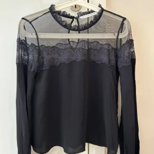 Svart spetsblus från Zara Trafaluc - Supersnygg svart blus från Zara Trafaluc med transparent mesh upptill och vacker spetsdetalj längs halsringning och axlar. Långärmad modell med rund hals och knäppning bak i nacken. Perfekt för dig som gillar en stilren men ändå romantisk look.