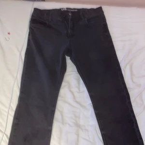 Svarta jeans från LAB Industries - Svarta jeans från LAB Industries i storlek 164. Klassisk femficksmodell med raka ben och normal passform. Snygga och stilrena, perfekta till en avslappnad look. Jeansen har diskreta sömmar och dragkedja i gylfen.