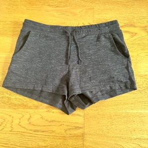 Svarta shorts med snörning - Svart shorts i mjuk bomull med diskret melerad look. De har elastisk midja med snörning och två sidofickor. Perfekta för chill dagar eller träning. Snygg och enkel design som är lätt att matcha.