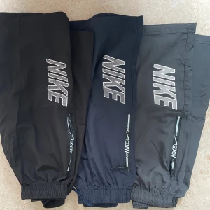 Nike träningsshorts med dragkedja för 10-13 åringar - Snygga träningsshorts från Nike i svart och mörkblått med stora logotyper på benet och dragkedjeförsedda fickor. Shortsen har elastisk midja med snörning och är tillverkade i lätt syntetmaterial, perfekta för sport eller chill. Klassisk sportig look med Nike Swoosh-detaljer.