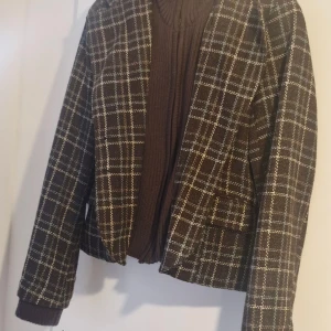 Rutig brun kavaj från Vila, stl M - Snygg rutig kavaj från Vila i brunt med inslag av vitt och grått. Klassisk rak modell med långa ärmar och mjukt tyg. Perfekt för dig som vill ha en stilren och trendig look. Fodrad insida och diskreta fickor framtill.