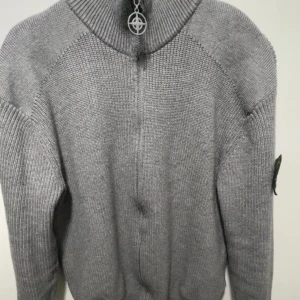 Grå stickad kofta från Stone Island - Säljer en grå stickad kofta från Stone Island med dragkedja och ikonisk patch på ärmen. Koftan har ribbade muddar, hög krage och snyggt metallhänge på dragkedjan. Perfekt för lager-på-lager och chill stil.