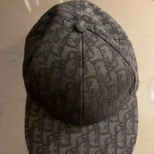 keps - Snygg mörkbrun keps med ett diskret rutigt mönster i tyget. Kepsen har klassisk form med böjd skärm och paneler, perfekt för att lyfta din streetstyle. Materialet känns slitstarkt och har en lätt glansig finish.