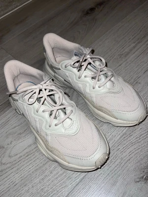 Beige Adidas Ozweego sneakers - Strumpliknande passform. Knyts med snören. Ovandel i stickat material och syntetläder med överdrag i TPU. Mjukt, åtsittande och lätt material. Textilfoder EVA-mellansula med dämpande Adiprene och Adiprene+. Gummiyttersula. Väl omhändertagna. 
