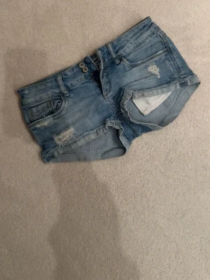 Ljusblå jeansshorts - Säljer ett par ljusblå jeansshorts med slitna detaljer. Dom är i bra skick och perfekta till sommaren! Skriv för frågor och prisförslag. Midjemått: 35cm, grenhöjd: 15cm