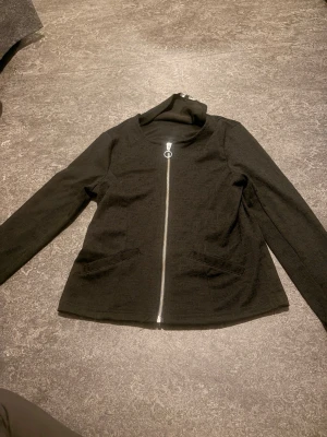 Svart cardiganjacka med dragkedja - Stilren svart cardigankofta med rund halsringning och silverfärgad dragkedja framtill.Perfekt för lager på lager och enkel att matcha med olika outfits.   Den har ej fickor endast detaljer