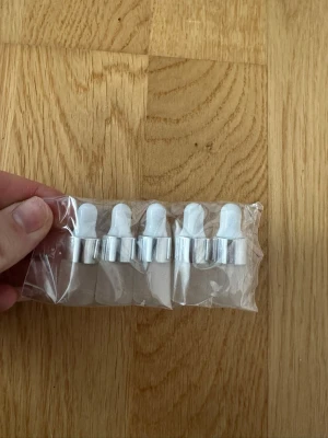 Vita pipetter med silverdetalj 5-pack - Fem stycken vita pipetter med silverfärgade ringar, perfekta för att dosera oljor, serum eller andra skönhetsprodukter. Tillverkade i plast och metall, levereras i en genomskinlig plastpåse. Smidig storlek för resor eller hemmabruk.