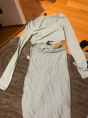 Ljusblått ribbat set från SHEIN - Säljer ett ljusblått ribbat set från SHEIN i storlek XS. Setet består av en långärmad crop top med rund halsringning och en matchande kjol med resår i midjan. Materialet är stretchigt och mjukt, perfekt för en trendig look.