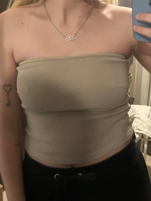 Beige tubtopp - Snygg beige bandeau tubtopp. Toppen är croppad och sitter tight runt kroppen, perfekt för en trendig och enkel look. Passar till både jeans och kjol för en chill stil.
