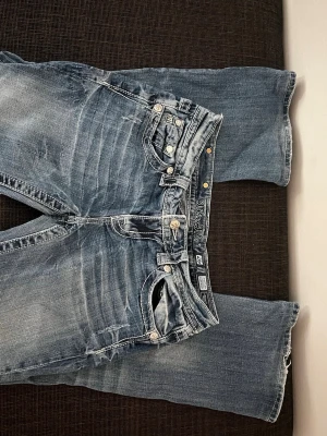 Blåa Miss Me shorts med broderi - Säljer ett par blåa jeansshorts från Miss Me med snyggt slitna detaljer och stora broderade fickor bak med pärlor och paljetter. Shortsen har normal passform och är gjorda i bomullsmaterial. Perfekta för dig som vill sticka ut lite extra i sommar!