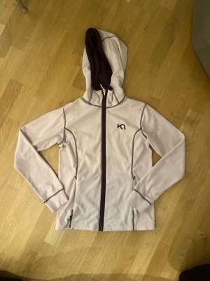 Ljuslila hoodie från Kari Traa - Säljer en ljuslila hoodie från Kari Traa med dragkedja framtill och mörklila detaljer. Hoodien har en fodrad huva, två fickor med dragkedja och dekorativa sömmar. Perfekt för chill dagar eller träning.