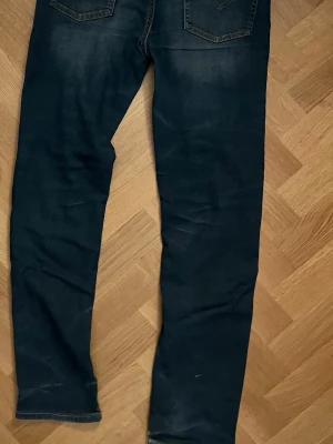 Mörkblå slim fit jeans - Snygga mörkblå slim fit jeans med klassisk femficksdesign och lätt slitna detaljer. Jeansen har normal midja och raka ben, perfekta till en avslappnad stil. 